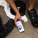 Person holding a 'RISE' supplement container next to black cycling shoes on a concrete floor.