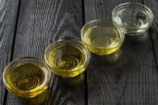 Four bottles of alternative cooking oils—avocado, flaxseed, grapeseed, and walnut oil—lined up on a kitchen counter, promoting heart-healthy cooking choices.