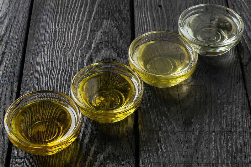 Four bottles of alternative cooking oils—avocado, flaxseed, grapeseed, and walnut oil—lined up on a kitchen counter, promoting heart-healthy cooking choices.