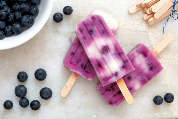 A colorful assortment of seven delicious summer popsicles in various flavors and vibrant colors, displayed on a wooden board with fresh fruit and herbs around, showcasing refreshing treats perfect for all ages to enjoy during hot weather.