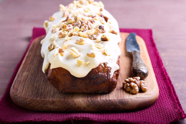 Image of a vegan pumpkin walnut loaf topped with creamy spiced buttercream frosting, garnished with whole walnuts and a sprinkle of cinnamon, served on a rustic wooden board.