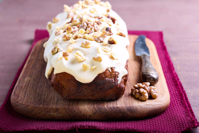 Image of a vegan pumpkin walnut loaf topped with creamy spiced buttercream frosting, garnished with whole walnuts and a sprinkle of cinnamon, served on a rustic wooden board.