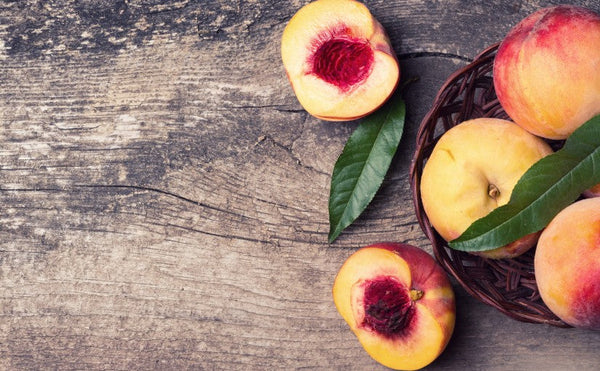 A vibrant flat lay of seven peach-inspired dishes, including peach salad, grilled peaches, and peach cobbler, surrounded by fresh, sun-ripened peaches and herbs on a rustic table.