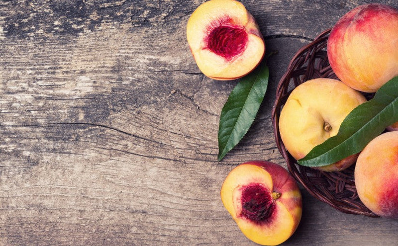 A vibrant flat lay of seven peach-inspired dishes, including peach salad, grilled peaches, and peach cobbler, surrounded by fresh, sun-ripened peaches and herbs on a rustic table.