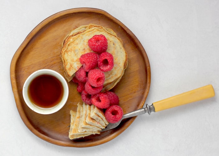 Fluffy raspberry protein pancakes stacked high on a plate, topped with fresh raspberries and drizzled with maple syrup, perfect for a healthy and delicious breakfast.