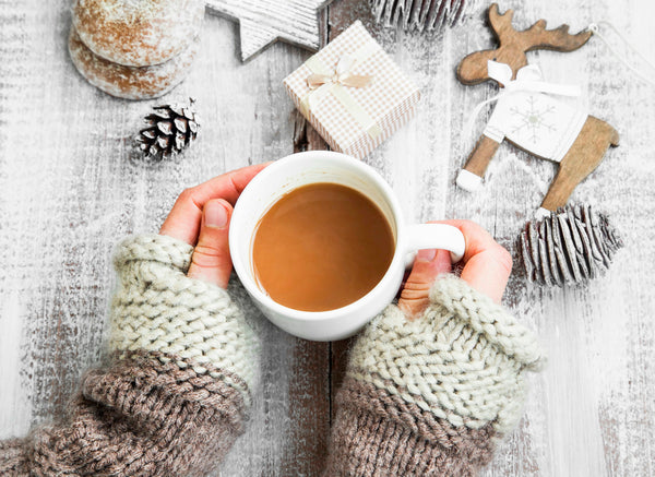 Creamy vegan holiday nog served in a glass with cinnamon sticks and festive lights in the background.