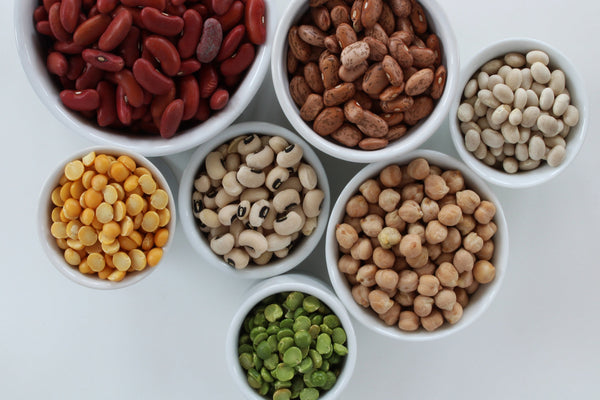 Assorted vegan protein sources including lentils, quinoa, tofu, and chickpeas on a wooden table.