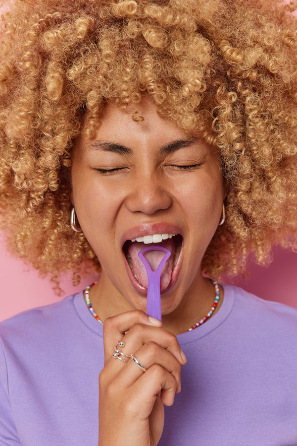 Close-up of a person using a tongue scraper to remove buildup for better oral hygiene.