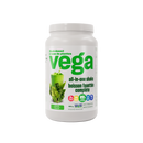 Blended Vega shake in a glass with creamy texture, placed beside the product tub and a spoonful of powder.