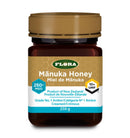 Jar of Flora Manuka Honey 250+ MGO / 10+ UMF placed on a wooden table with honey dipper and natural flowers, highlighting its premium New Zealand origin.