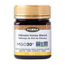 A jar of Flora Manuka Honey Blend with a label indicating it is MGO30+ and has a net weight of 250g. The jar has a golden lid and is recyclable PET.