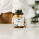 Angled view of Flora Super 8 Plus Probiotic bottle with transparent VCaps container partially open, capsules spilling out on a wooden surface next to fresh mint leaves.