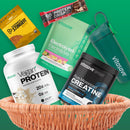 A basket containing various athletic supplements including vegan protein powder, creatine, electrolytes, a shaker bottle, and a protein bar.