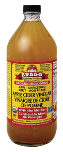 Close-up of Bragg Apple Cider Vinegar bottle next to fresh apples on a wooden surface.